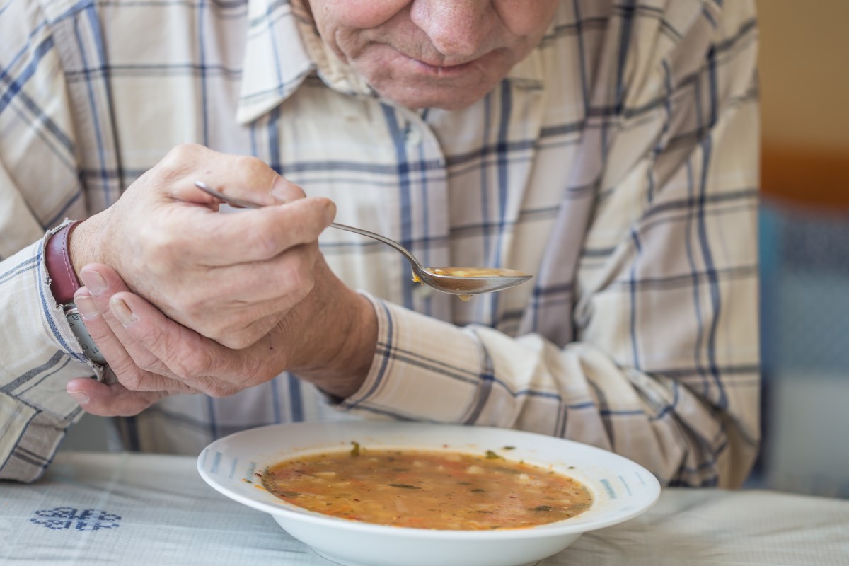 Moški poje juho in drži roko proti tresenju pri Parkinsonovi bolezni