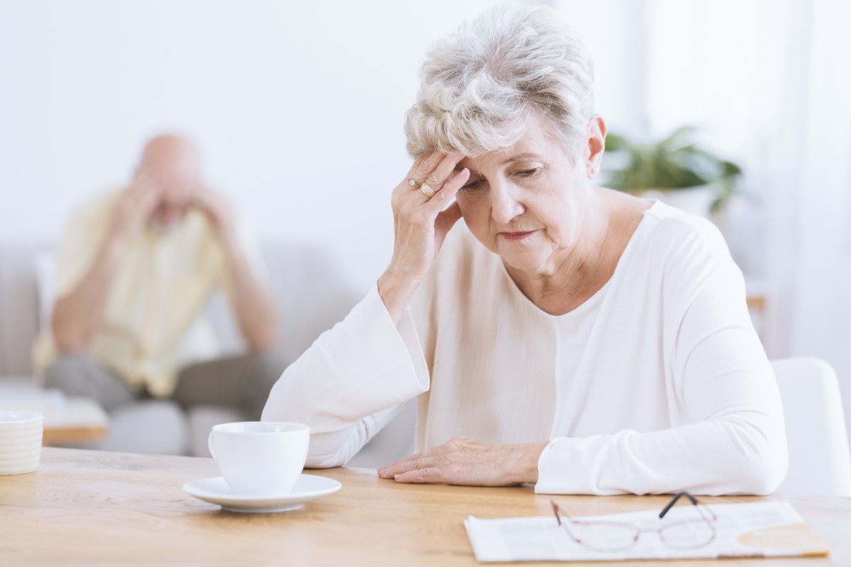 Starejša ženska se drži za glavo zaradi poslabšanja nevroloških funkcij možganov, morda Alzheimerjeve bolezni. Starejša ženska v ospredju s sklonjeno glavo, naslonjena na roko