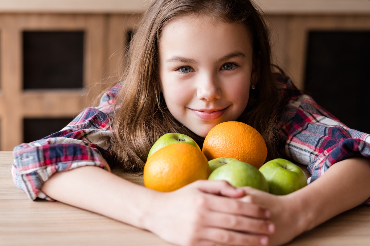 Vitamin C v sadju, otrok s pomarančami in jabolki v rokah