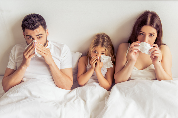 Družina, tj. oče, mati in hči ležijo v postelji, imajo polne nosove, so prehlajeni, zaradi bolezni, na primer gripe.